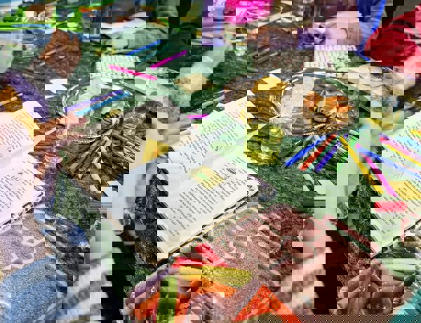 Foto af grøn dug med en bog og en tallerken med gifler og kiks. Eleverne spiser mens de læser.